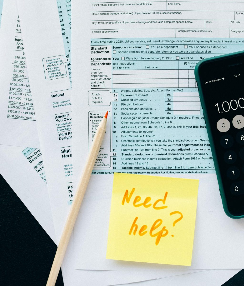 Close-up of tax forms with a calculator and a note asking for assistance.